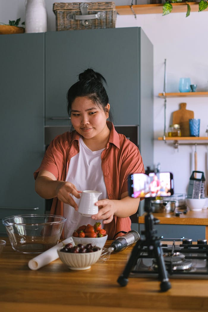 services-img-01 Asian woman filming a cooking tutorial in a modern kitchen, using fresh ingredients.