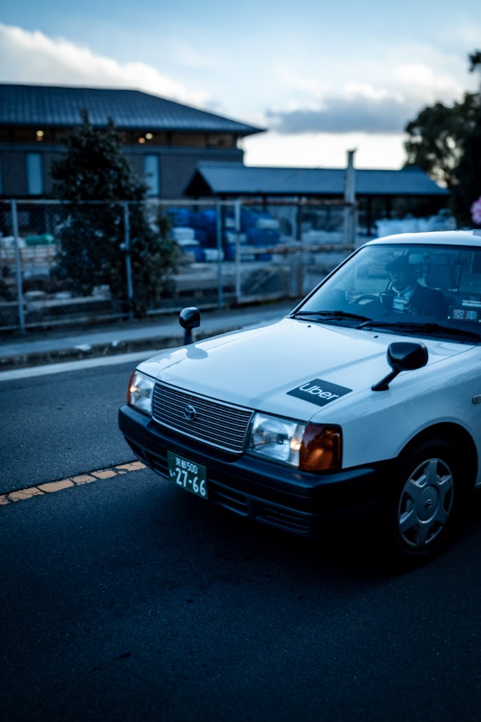 our-story White taxi with Uber sign on a Kyoto street at dusk, featuring traditional buildings.